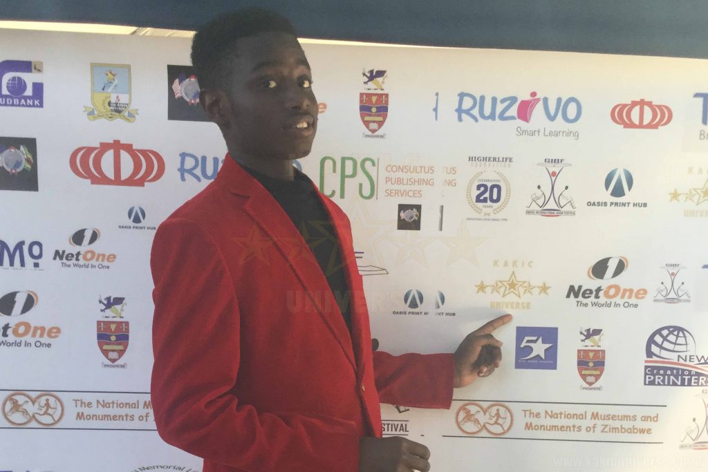 Kudakwashe Maxwell posing infront of the banner of participants at the GIBF 2017